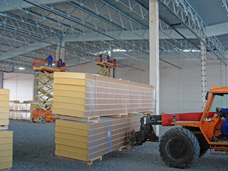 Warehouse construction, installation work on scissor lifts. Fork loader lifts a pack of sandwich...
