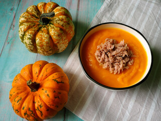 on a blue wooden table there is a gray round plate of pumpkin cream soup with tuna next to two small pumpkins.  gluten-free, vegan.  diet.  view from above.  menu calendar