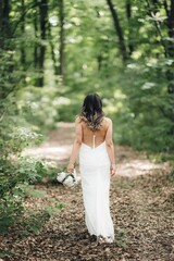 Bride holding a bouquet walking through a lush forest.