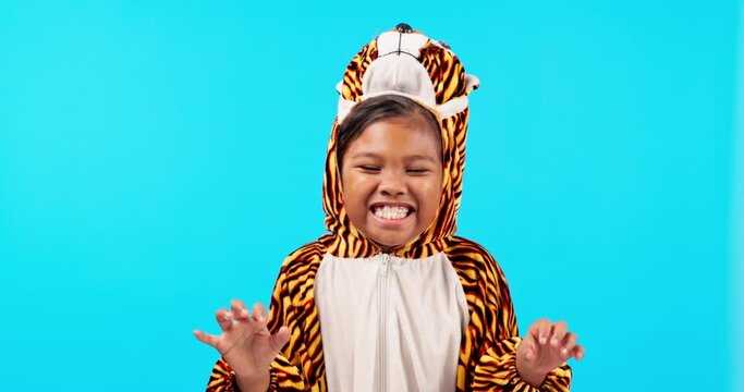 Tiger costume, roar and face of girl in studio with halloween onesie for fun, playful and playing. Childhood, blue background and portrait of child with crazy, goofy and silly expression for scare