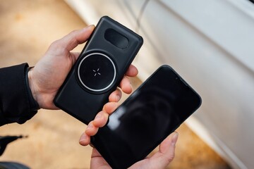 Closeup of the hands of a person holding a smartphone and a wireless phone charger