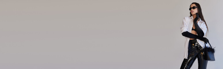 bold style, fashion statement, asian woman in sunglasses posing with feathered handbag on grey background, young model in latex shorts, black gloves and white shirt, conceptual, banner