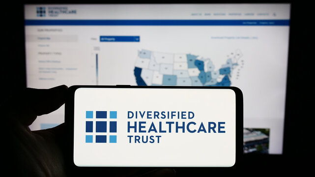 Stuttgart, Germany - 06-18-2023: Person holding smartphone with logo of real estate company Diversified Healthcare Trust on screen in front of website. Focus on phone display.