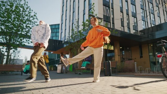 Two Professional Hip Hop Dancers Jamming On City Street Among Modern Buildings. Male And Female Street Style Performers Freestyling Downtown, Friends Supporting and Livestreaming Via Smartphone.