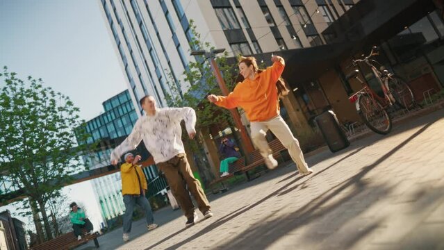Two Professional Hip Hop Dancers Jamming On City Street Among Modern Buildings. Male And Female Newstyle Performers Freestyling Downtown, Stylish Friends Supporting, Livestreaming Via Smartphone.