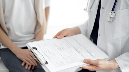 Doctor and child patient. The physician is holding clipboard with medication history records form near a boy. The concept of ideal health in medicine