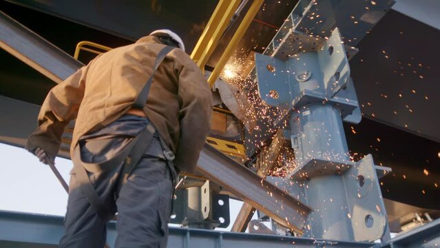 Slow-motion view of a construction worker standing under welding sparks