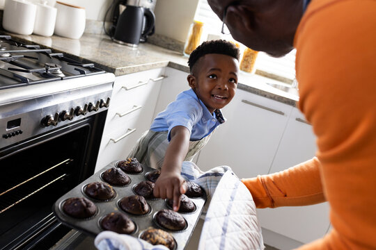 Happy african american grandfather and grandson baking in kitchen, slow motion