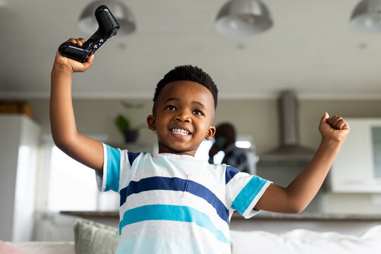 Happy african american boy sitting on sofa and playing video games