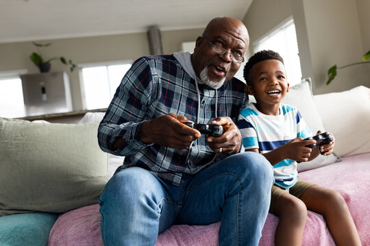 African american grandfather and grandson sitting on sofa and playing video games