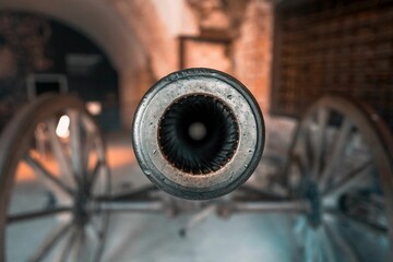 Antique metal cannon placed next to a brick wall with its accompanying wheels.