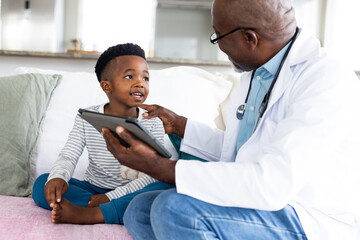 Senior african american male doctor using tablet talking to boy patient