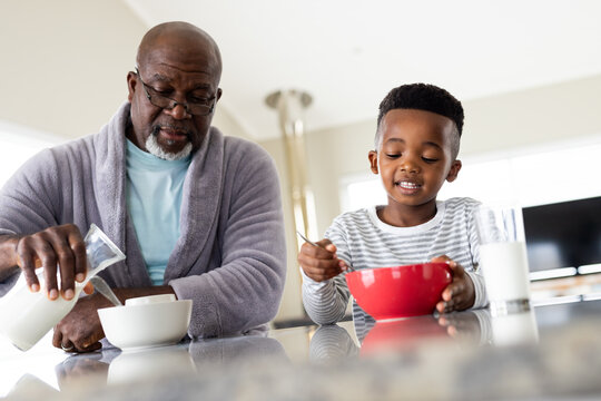 Happy african american grandfather and grandson eating breakfast in kitchen - Powered by Adobe