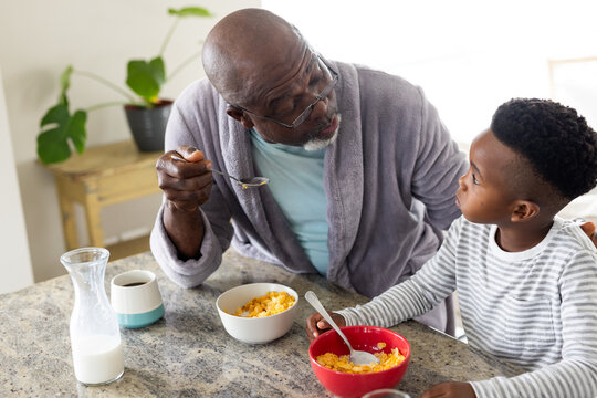 Happy african american grandfather and grandson eating breakfast in kitchen