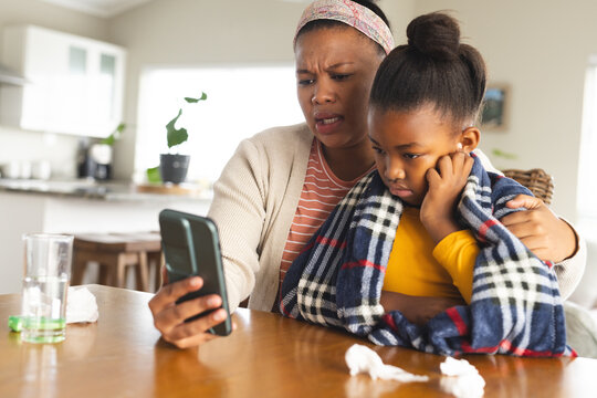 African american mother and daughter using smartphone for online consultation with doctor