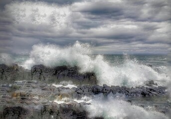 Waves crashing onto the rocky shoreline beneath a cloudy sky on the Isle of Skye. - Powered by Adobe