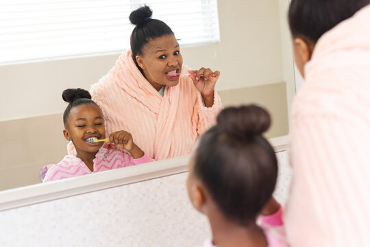 African american mother and daughter brushing teeth in bathroom