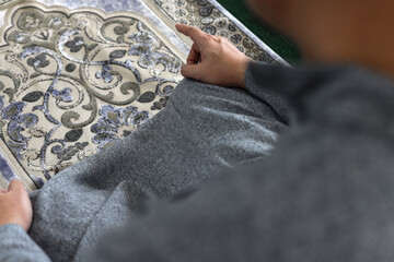 Close up muslim man praying on prayer mat doing last movement on salat procedure. The worshiper proceeds to sit and recite the tashahhud