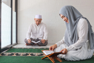Blurry image of muslim woman and her husband reciting Quran during Ramadan month in mosque