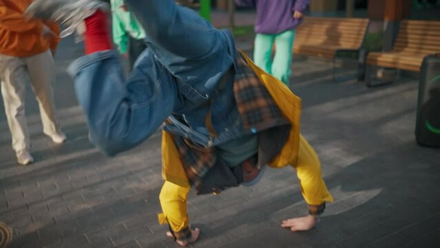 Dynamic Shot of Young And Athletic B-Boy Breakdancing To Break Beats On The City Street Among Modern Buildings In The Circle Of Friends. Fashionable People Supporting Dancer, Filming On The Smartphone