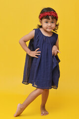A full length shot of adorable little Asian girl wearing dress standing hands at the waist, isolated on yellow background.