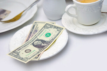 top view close-up on white plate with American dollars bills and coins, selective focus, cup of coffee, dishes with food, lunch concept in restaurant, cafe, tip money concept, change of waiter