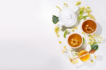 Organic herbal health drink. Linden plant flower green tea, in white mugs, with a teapot, on a white table, with copy space and blooming linden inflorescences and flowers