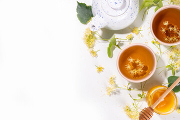 Organic herbal health drink. Linden plant flower green tea, in white mugs, with a teapot, on a white table, with copy space and blooming linden inflorescences and flowers