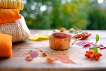 Autumn composition on rustic wooden table in garden with hot tea, coffee in mug, fallen yellow,...
