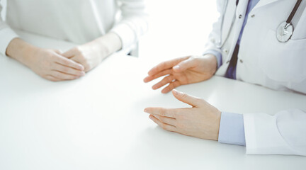 Doctor and patient discussing current health questions while sitting near of each other at the table in clinic, just hands closeup. Medicine concept