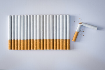Cigarettes lined up on a white colored plane, the last cigarette is broken, stop smoking concept.