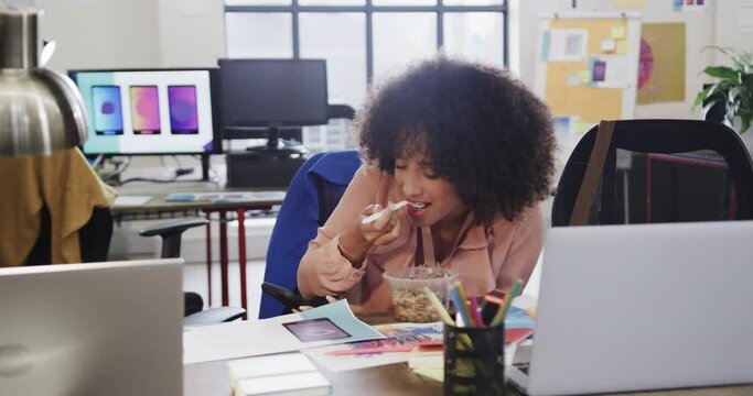 African american female designer using smartphone during lunch in casual office, slow motion