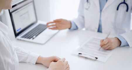 Doctor and patient using tablet computer while sitting opposite each other at the desk in clinic. The focus is on female hands near physician, close up. Medicine concept