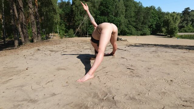 Rear view of a sporty young woman in a black swimsuit on the sand doing stretching. Beautiful workout woman. Long hair woman workout
