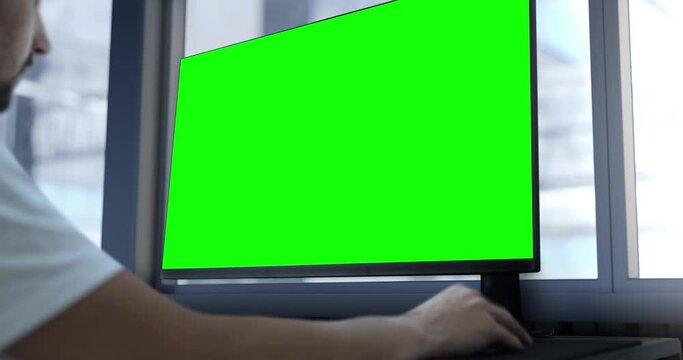An engineer works on a computer with a green screen. In the background, there is a production hall, a template for work in a design facility in the technological, mechanical, or IT industry