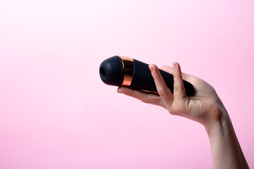 Female hand is holding black vacuum clitoral stimulator on a pink background. Place for text. Sex shop concept. Copy space
