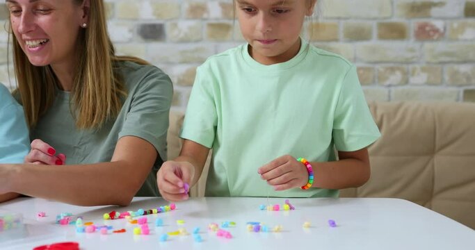 Happy mother with her daughters making beaded jewelry at home