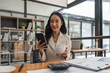 Obraz premium Pretty young business woman sitting on workplace. Smiling business woman. young business woman on the phone at office. Business woman texting on the phone and working on laptop