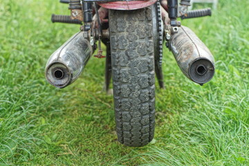 part of iron rusty dirty old chrome exhaust pipes with old motorcycle wheel of retro old motorbike on green grass outdoors at daytime