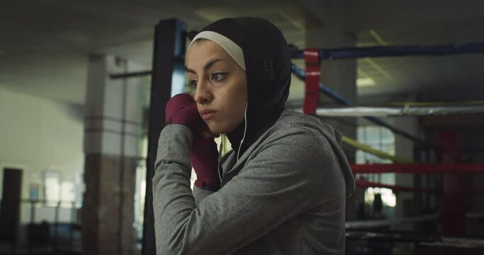 Slow Motion Portrait of Young Arab Woman with Earplugs Adjusting her Hijab Before Practicing Shadow Boxing in Gym. Strong Muslim Woman Working Out and Exercising, Throwing Punches with Confidence