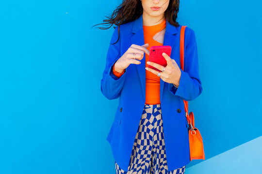 Woman surfing net using smart phone in front of blue wall