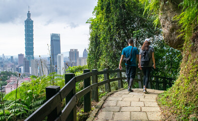 Obraz premium Young man and woman walking along path in park with Taipei skyline in the distance - Taipei, Taiwan