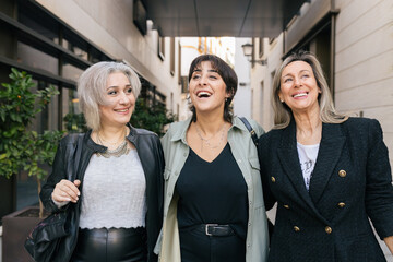 Cheerful women friends walking in the city, talking and smiling. Fashion street style trend for different aged woman