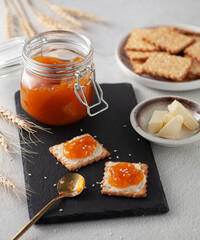 Breakfast crackers with butter and apricot jam on the board, jar of apricot jam, plate of crackers and butter. Selective focus