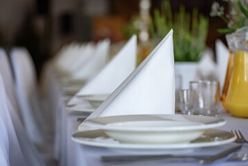 Biały stół ozdobiony białymi talerzami, serwetkami i kieliszkami do wina, ze sztućcami, ustawiony na imprezy - obrazy, fototapety, plakaty
