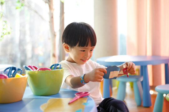 Multicolored art education materials, children's stationery and learning creative drawing and origami play, a cute child in a kindergarten classroom is smiling happily while looking at his creations.
