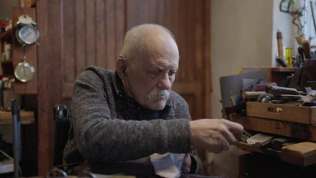 Senior gray haired male master in a wheelchair working at his workshop sharpening japanese swords blade