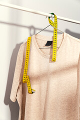 Beige t-shirt with measuring tape on wooden hanger, displayed on clothes rack.