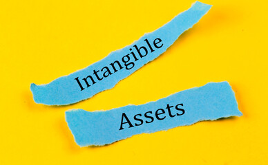 INTANGIBLE ASSETS text on a blue pieces of paper on yellow background, business concept