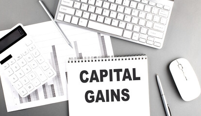 CAPITAL GAINS text written on notebook on grey background with chart and keyboard, business concept